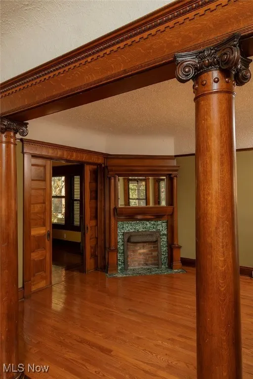 Entry to the living room featuring decorative columns, a textured ceiling, wood finished floors, and a high end fireplace