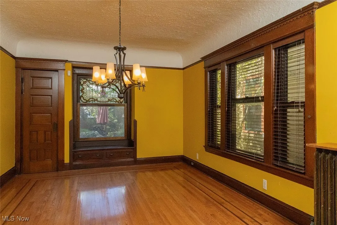 The dining area featuring a textured ceiling, wood finished floors, plenty of natural light, a chandelier, and radiator