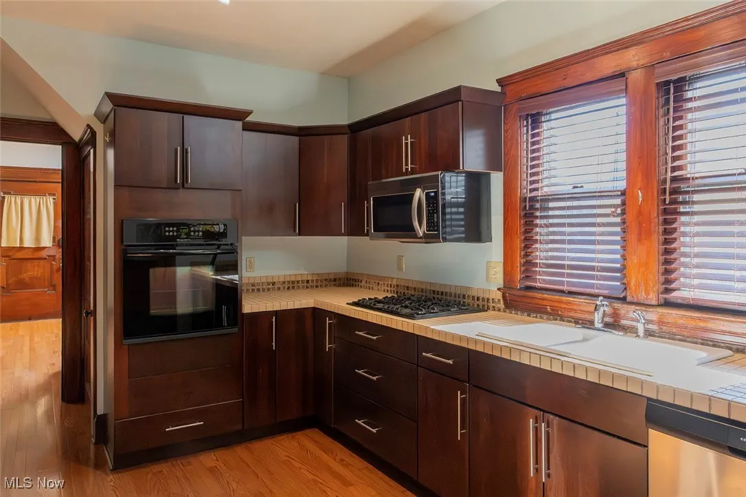 Kitchen featuring black appliances, dark brown wood cabinetry, and light wood finished floors