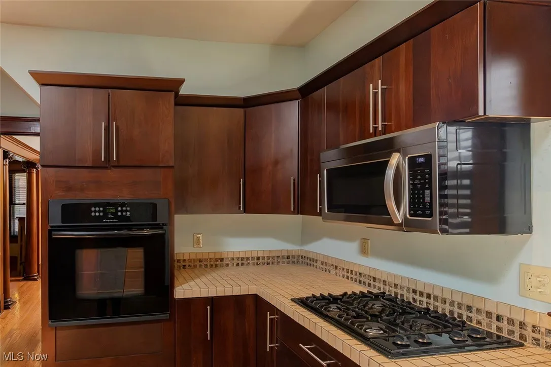 Kitchen featuring black appliances, light countertops, and dark brown wood cabinets