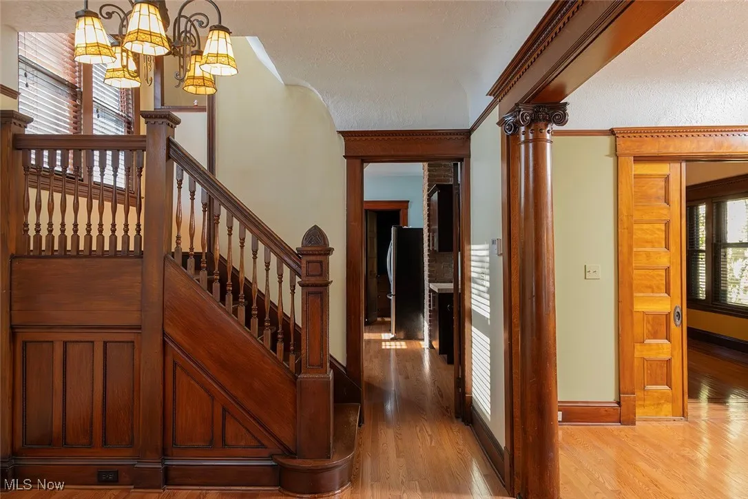 Hall featuring light wood finished floors, stairs, ornamental molding, a chandelier, and decorative columns