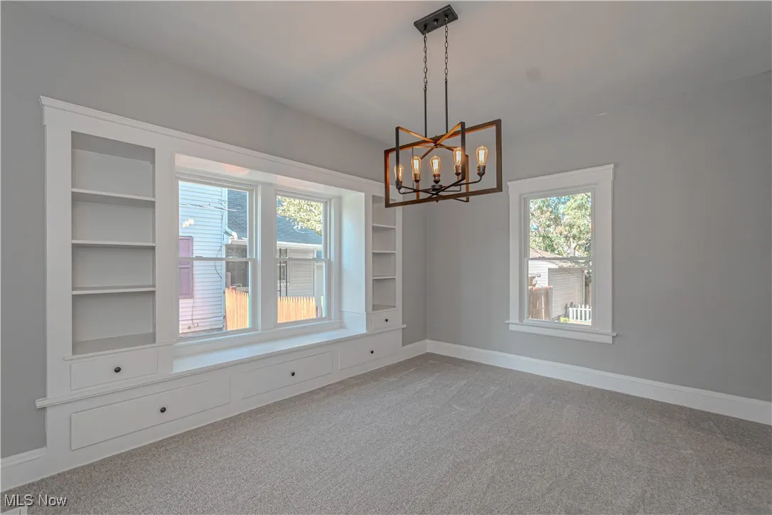 Empty room with carpet floors, a chandelier, and built in shelves