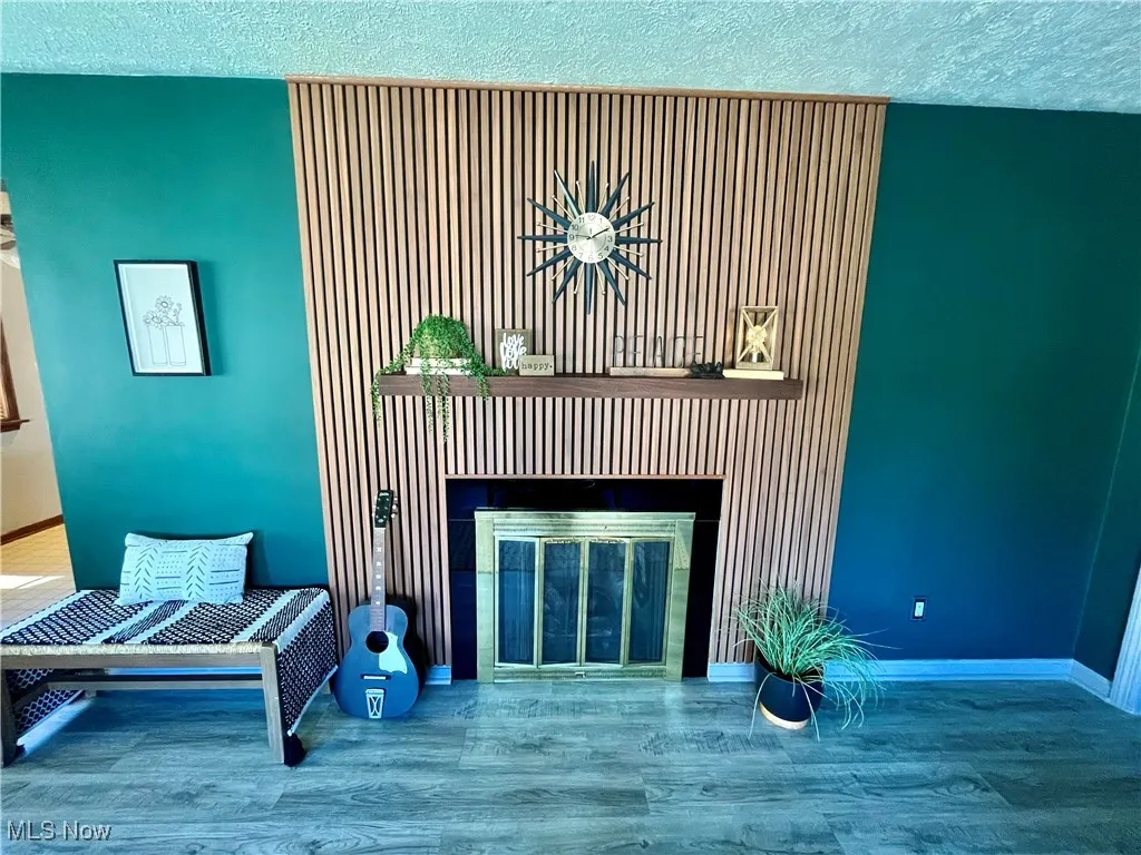 Detailed view of a textured ceiling, wood finished floors, and a glass covered fireplace