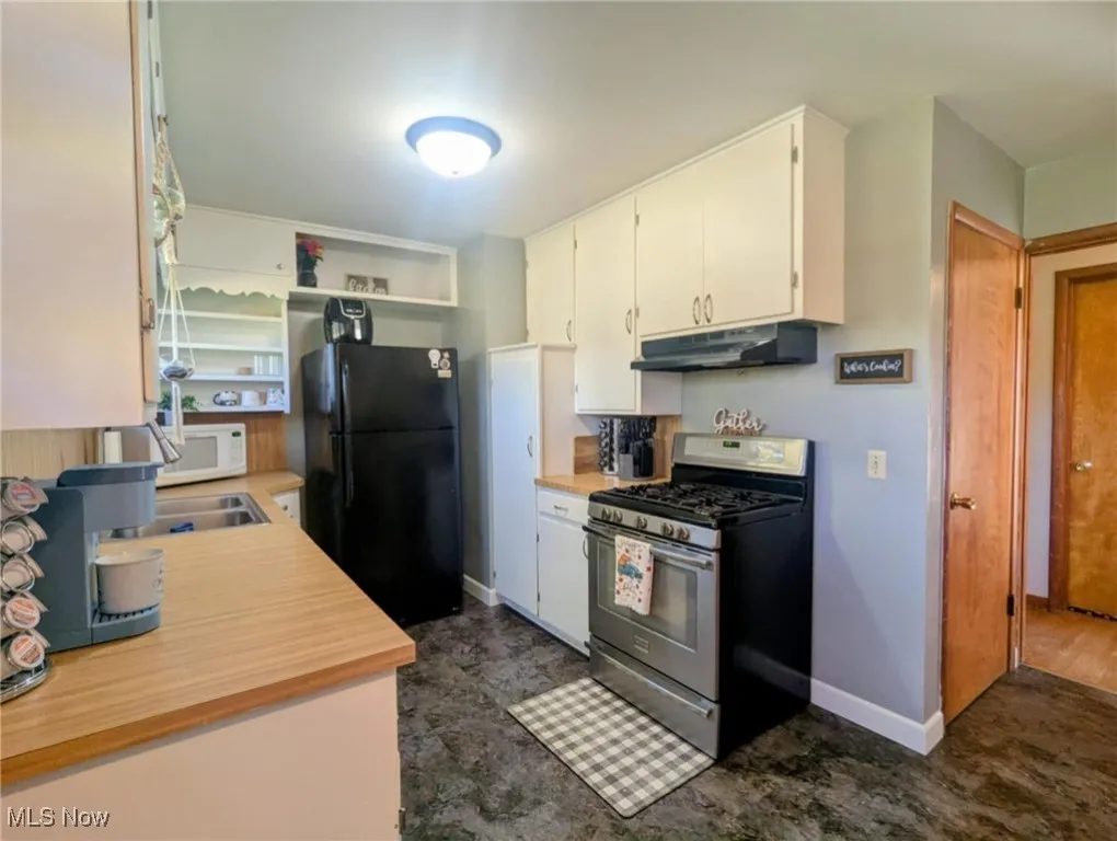 Kitchen featuring light countertops, stainless steel gas range oven, freestanding refrigerator, white cabinets, and under cabinet range hood