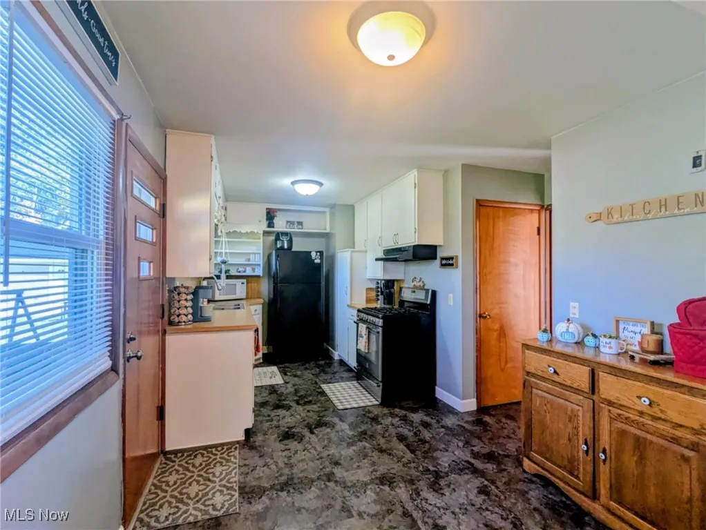 Kitchen with gas range, freestanding refrigerator, white cabinets, under cabinet range hood, and white microwave
