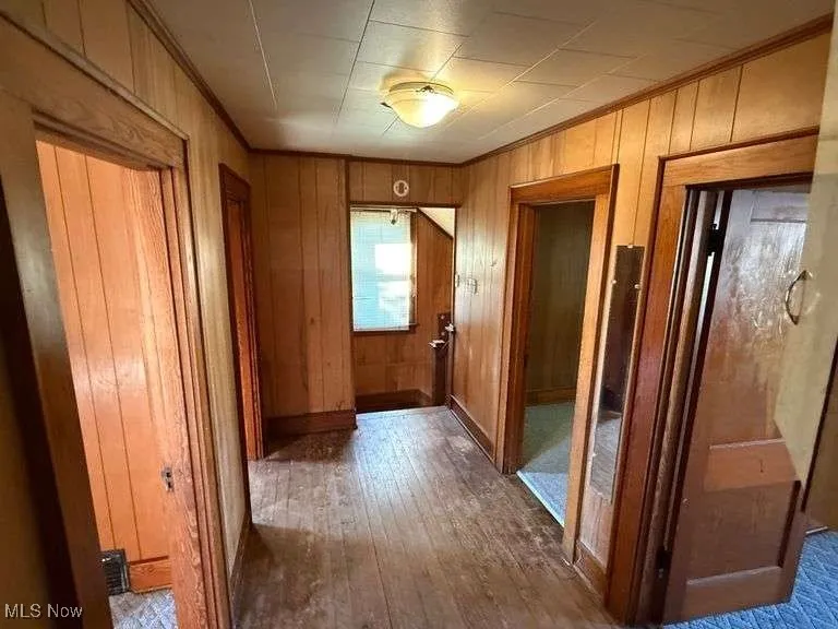 Corridor with dark wood-type flooring, wooden walls, and ornamental molding