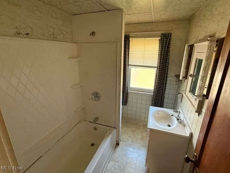 Bathroom featuring vanity, tile walls, shower / bathtub combination, and light flooring