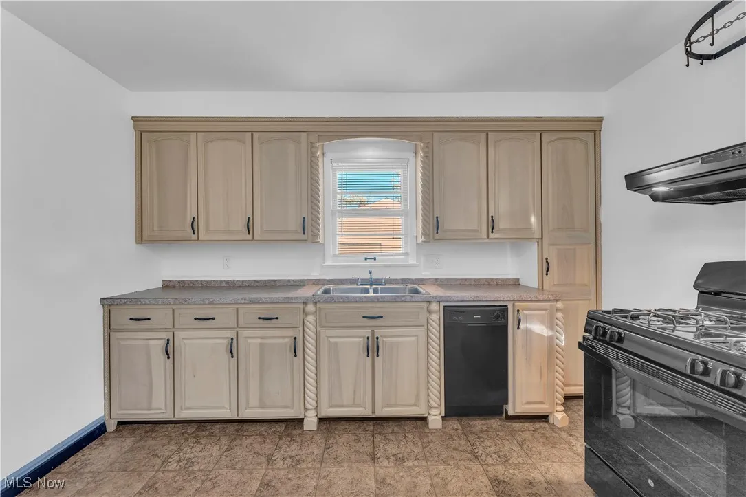 Kitchen featuring black appliances, range hood, light brown cabinets, and light countertops
