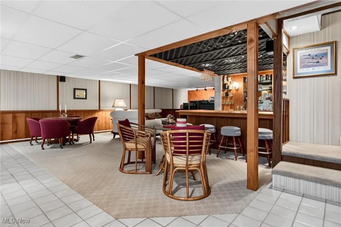 Dining room featuring tile patterned floors, a drop ceiling, bar area, wallpapered walls, and carpet flooring