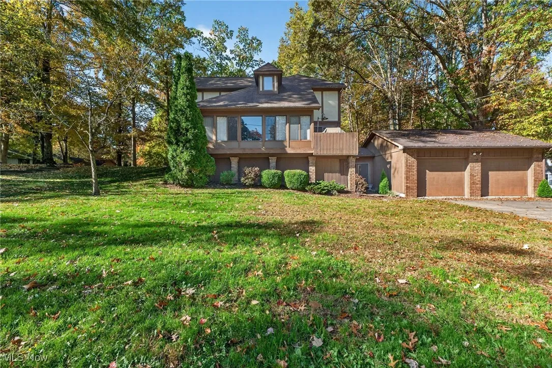 View of front of property featuring a garage, a front lawn, brick siding, and view of scattered trees
