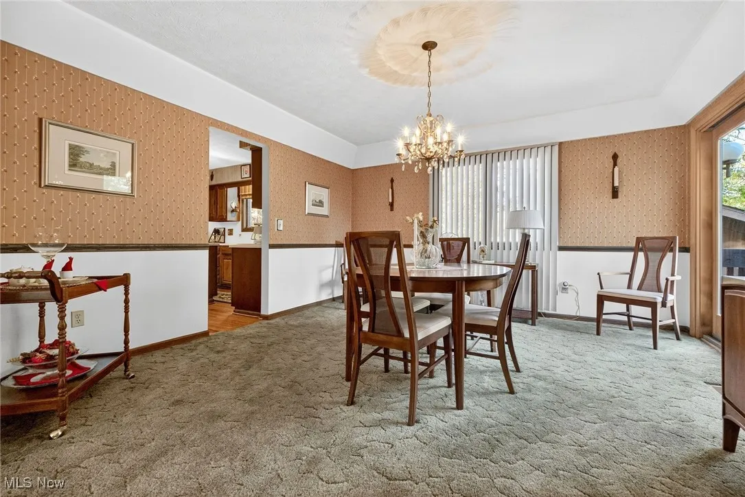Dining area featuring wallpapered walls, light colored carpet, a chandelier, and a wainscoted wall