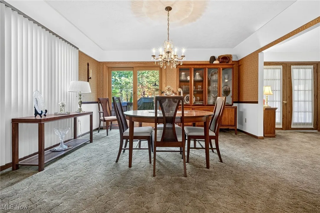 Carpeted dining space with wallpapered walls and a chandelier