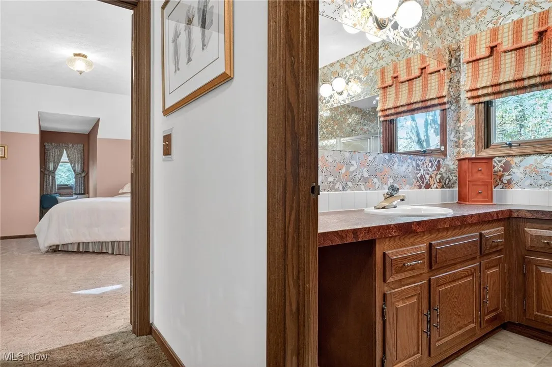 Ensuite bathroom featuring wallpapered walls, plenty of natural light, vanity, and light colored carpet