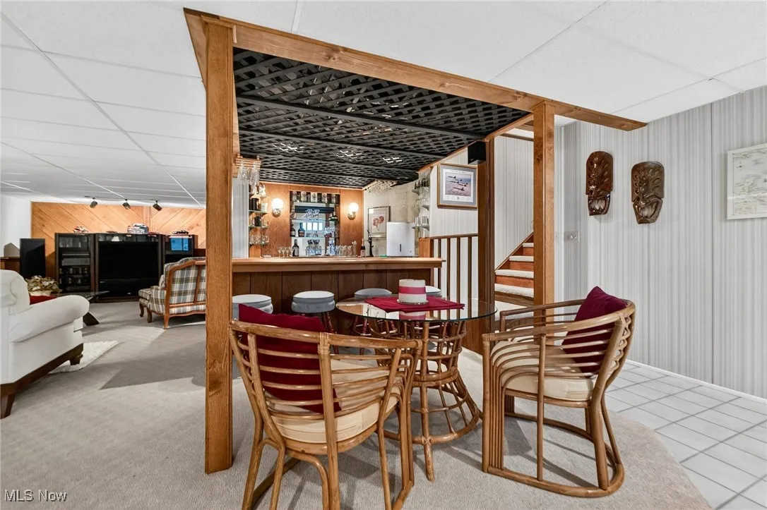 Dining area with a drop ceiling, wooden walls, a bar, tile patterned floors, and stairs