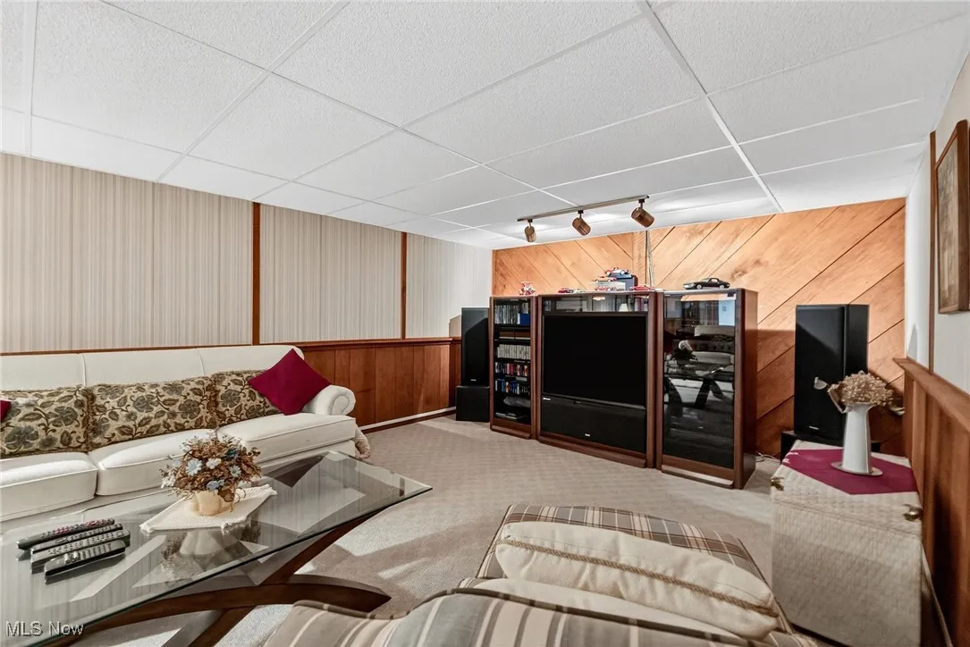 Living area featuring a paneled ceiling, carpet flooring, and wooden walls