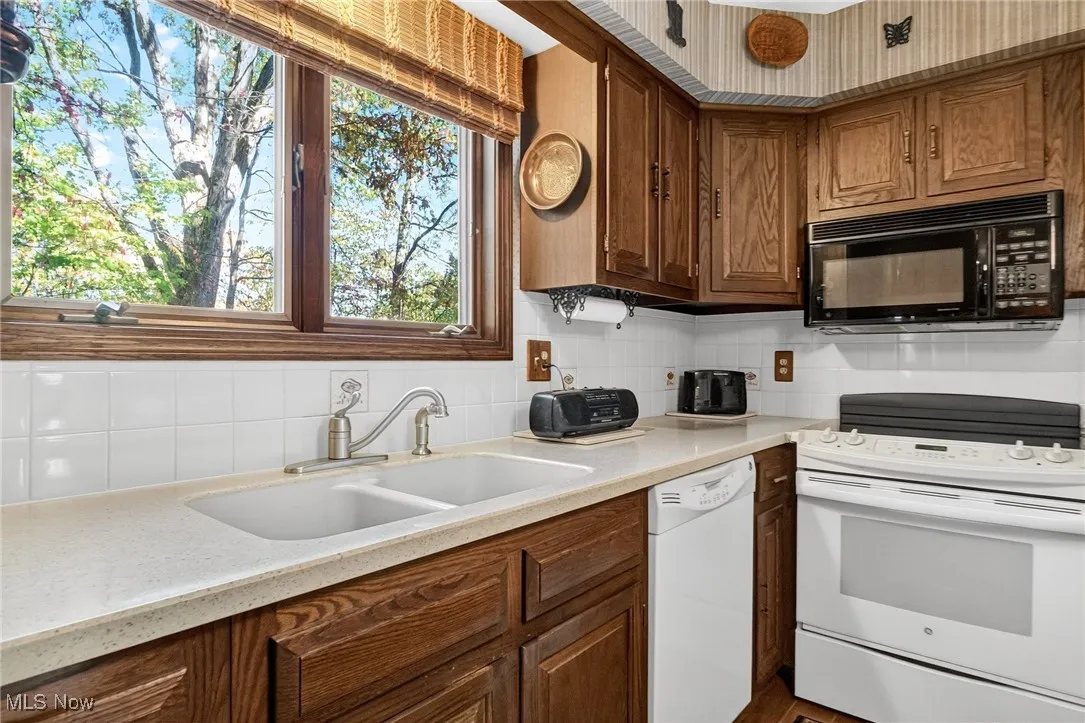 Kitchen featuring white appliances, tasteful backsplash, brown cabinets, and light stone countertops