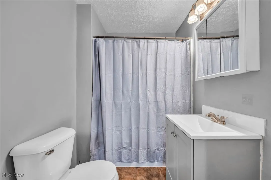 Full bath featuring a textured ceiling, vanity, and curtained shower