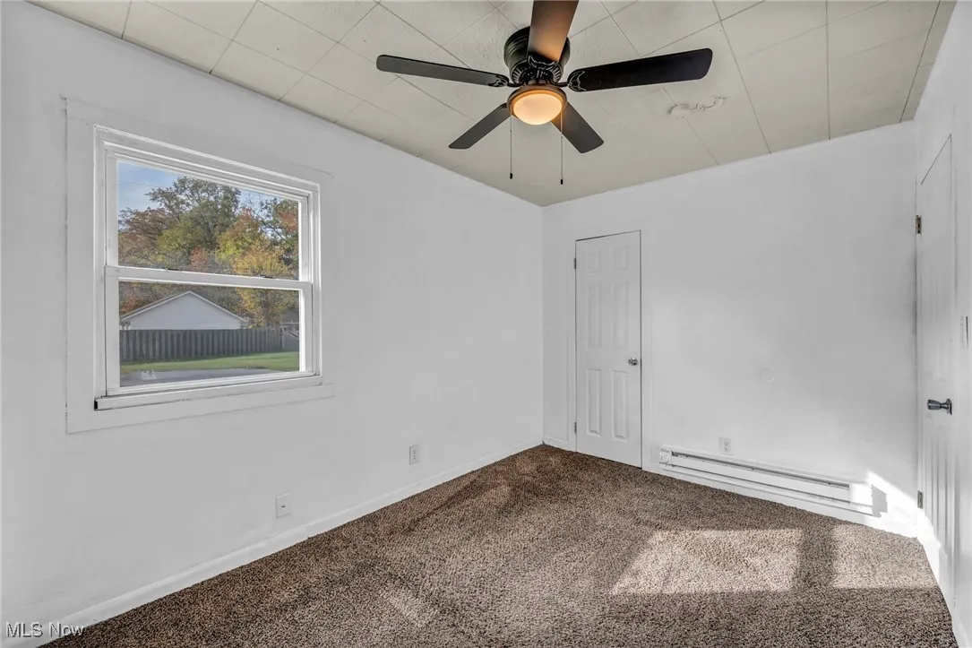 Unfurnished bedroom featuring carpet floors, a baseboard radiator, and ceiling fan
