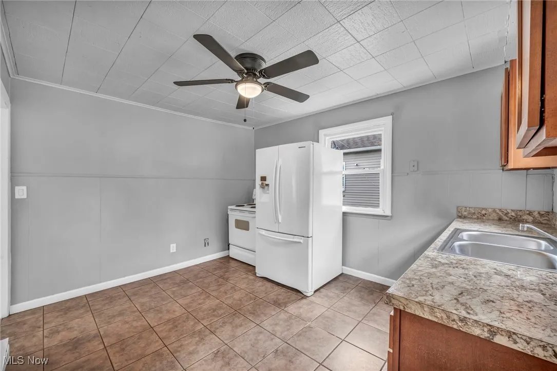Kitchen with white appliances, light countertops, wainscoting, light tile patterned floors, and ceiling fan