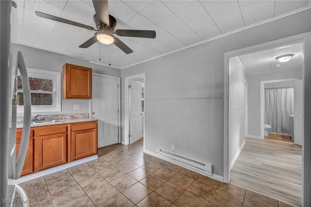 Kitchen with brown cabinets, light tile patterned flooring, baseboard heating, freestanding refrigerator, and crown molding