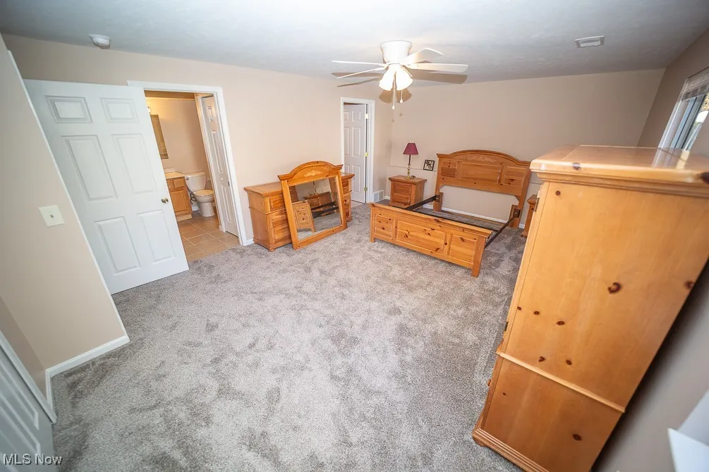 Bedroom featuring light carpet, ensuite bath, and a ceiling fan