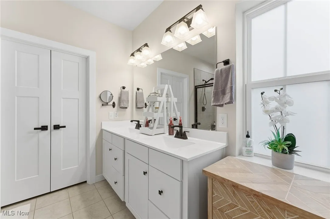Full bathroom featuring double vanity, light tile patterned flooring, and a stall shower