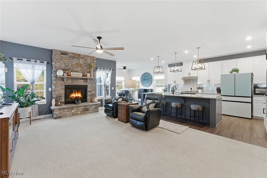 Living area with a stone fireplace, plenty of natural light, ceiling fan, and light wood-style flooring
