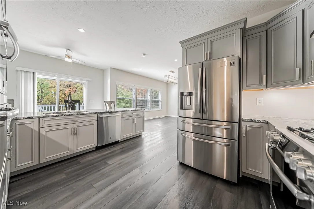 Kitchen with appliances with stainless steel finishes, light stone countertops, gray cabinets, recessed lighting, and dark wood-style flooring
