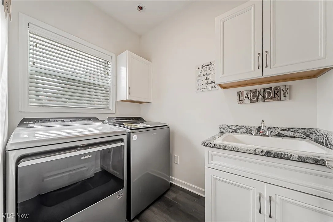 Laundry area with cabinet space, independent washer and dryer, and dark wood finished floors, window, and deep sink