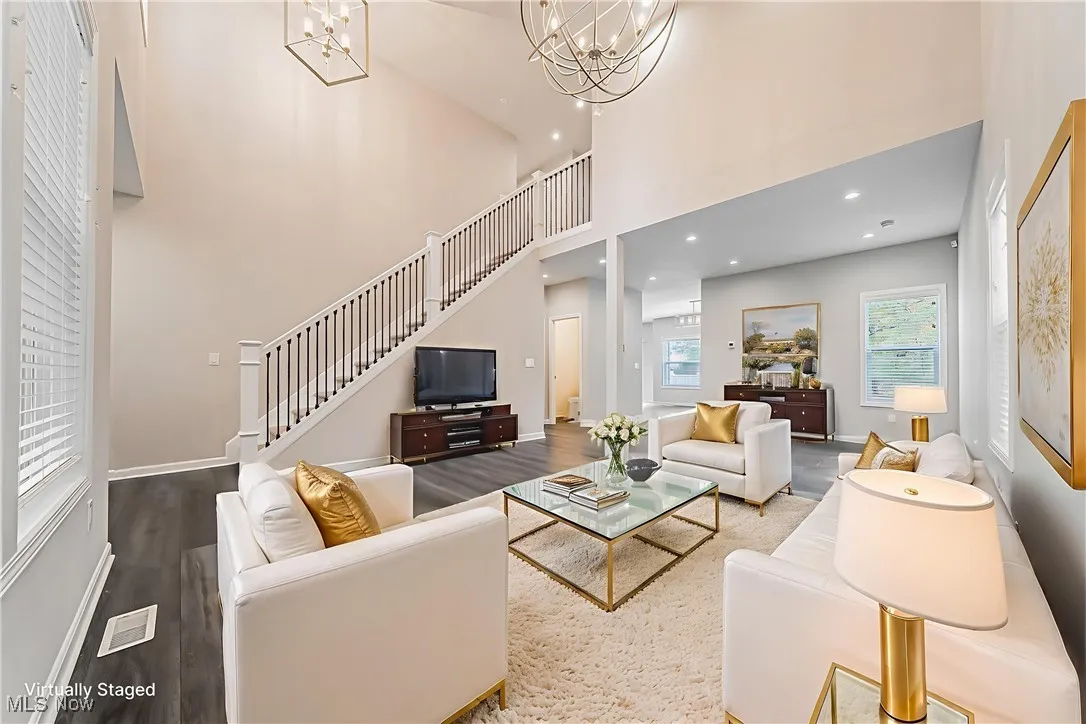 Virtually Staged-Living area featuring wood finished floors, recessed lighting, a towering ceiling, stairway, and a chandelier