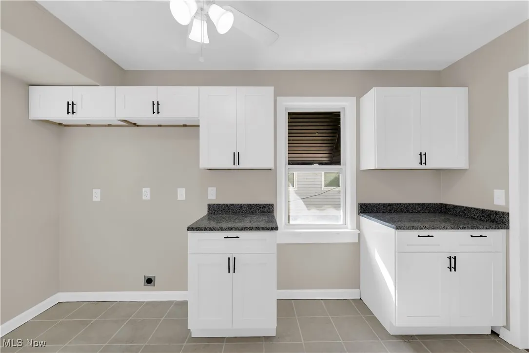 Kitchen with white cabinetry, light tile patterned flooring, ceiling fan, and dark stone countertops