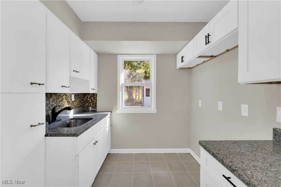 Kitchen featuring tasteful backsplash, white cabinets, light tile patterned floors, and dark stone counters