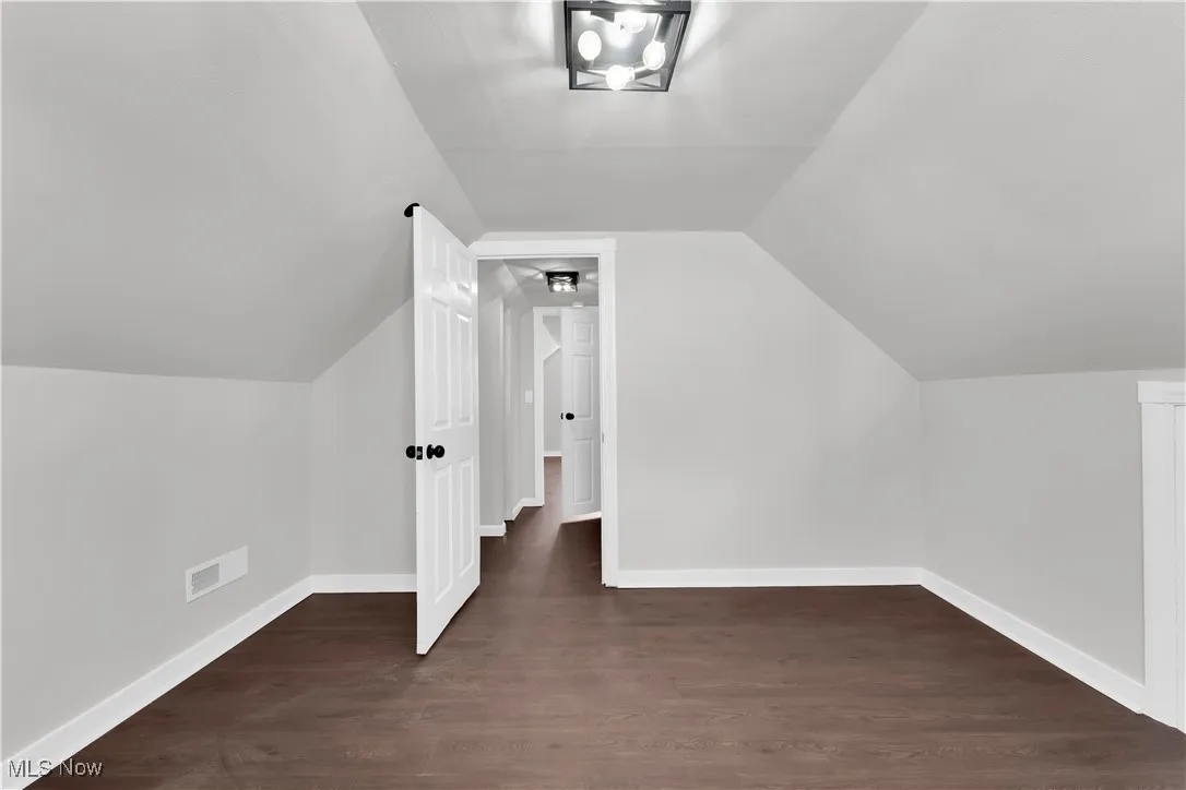 Bonus room with dark wood-type flooring and lofted ceiling