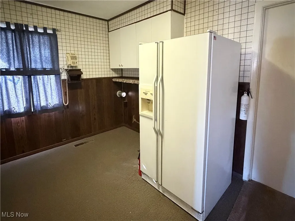 Kitchen featuring white refrigerator with ice dispenser, white cabinets, dark colored carpet, and tile walls