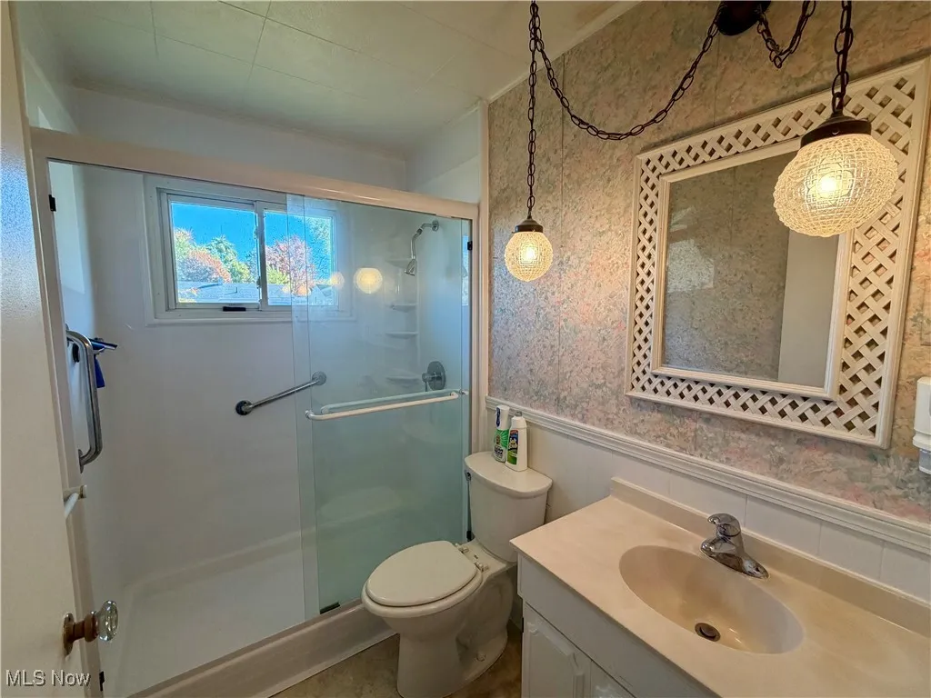 Bathroom with wallpapered walls, vanity, a wainscoted wall, and a shower stall