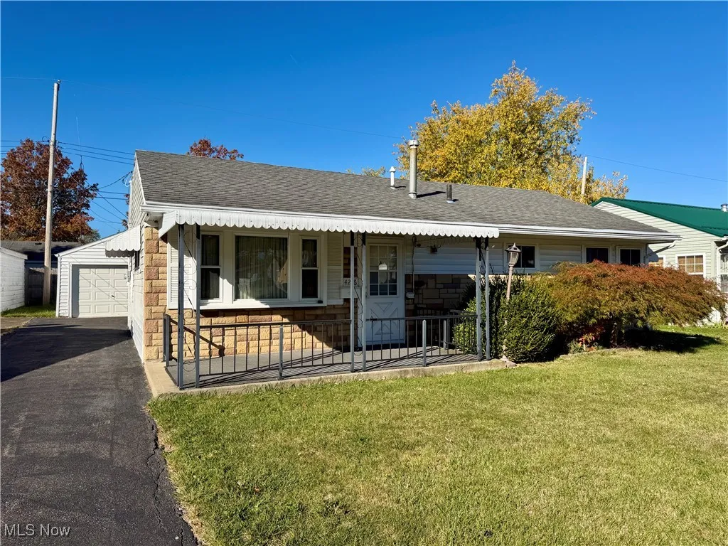 View of front of house with a shingled roof, a front lawn, stone siding, and covered porch