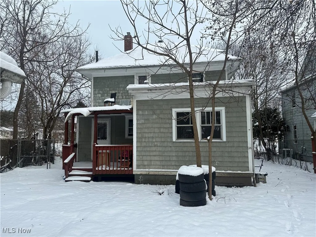 Snow covered house featuring a chimney and a wooden deck