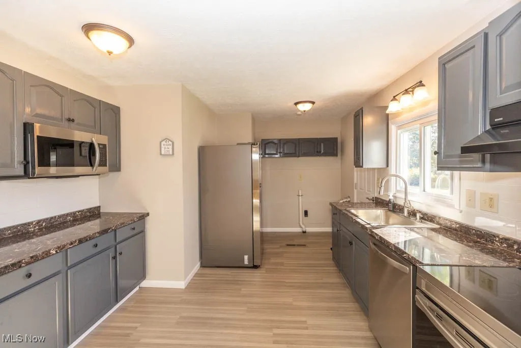Kitchen with stainless steel appliances, gray cabinets, dark stone countertops, tasteful backsplash, and light wood finished floors