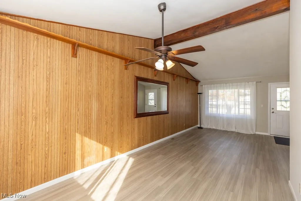 Empty room featuring wood finished floors, wooden walls, and a ceiling fan