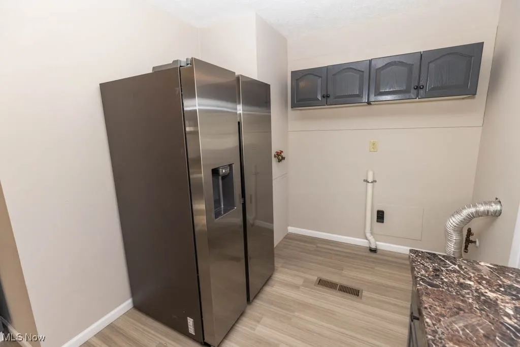 Kitchen with stainless steel fridge, light wood-style flooring, and dark stone countertops