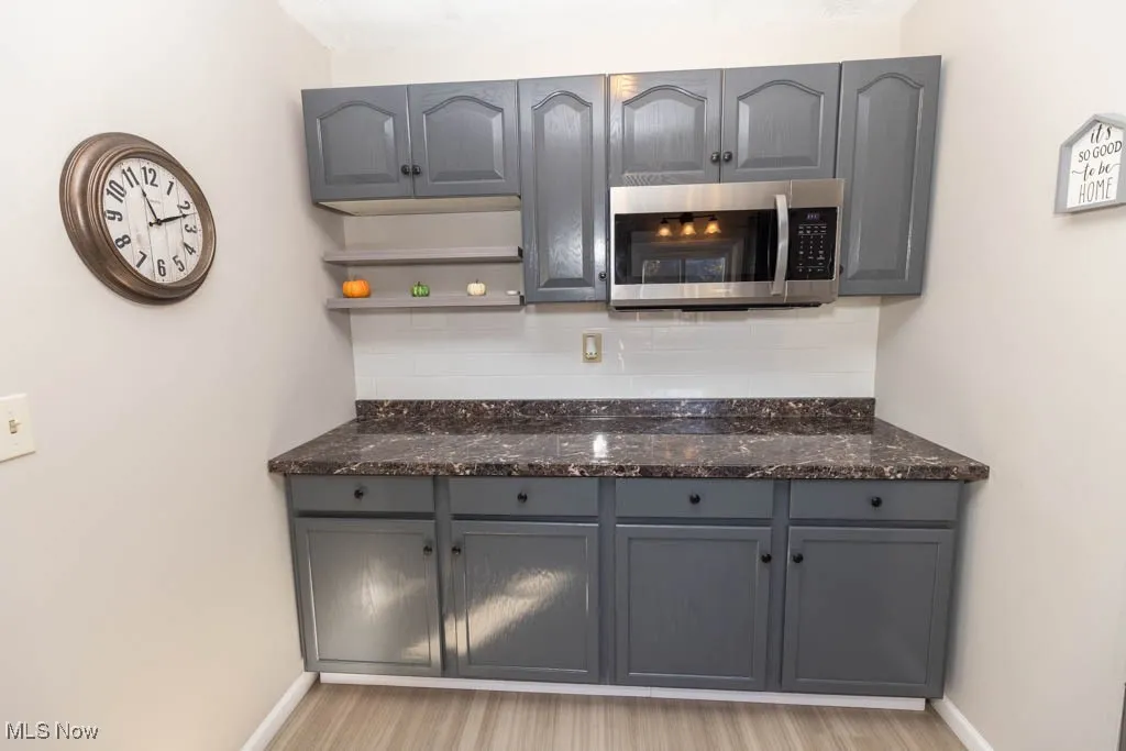 Kitchen featuring gray cabinetry, decorative backsplash, stainless steel microwave, dark stone counters, and light wood-style flooring