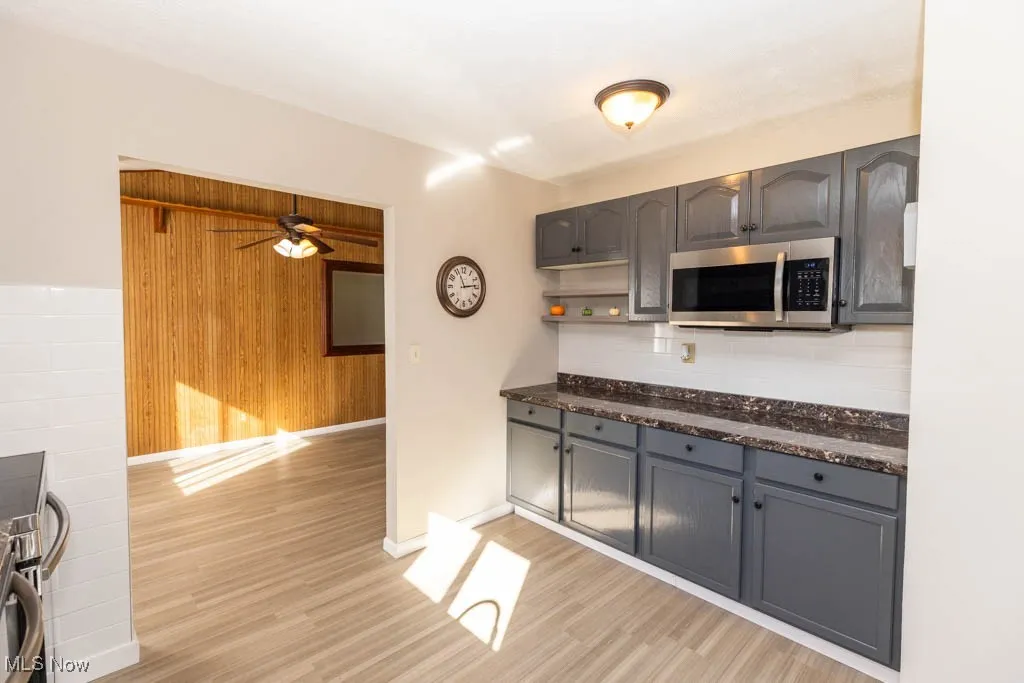 Kitchen with gray cabinetry, stainless steel microwave, open shelves, wooden walls, and light wood finished floors