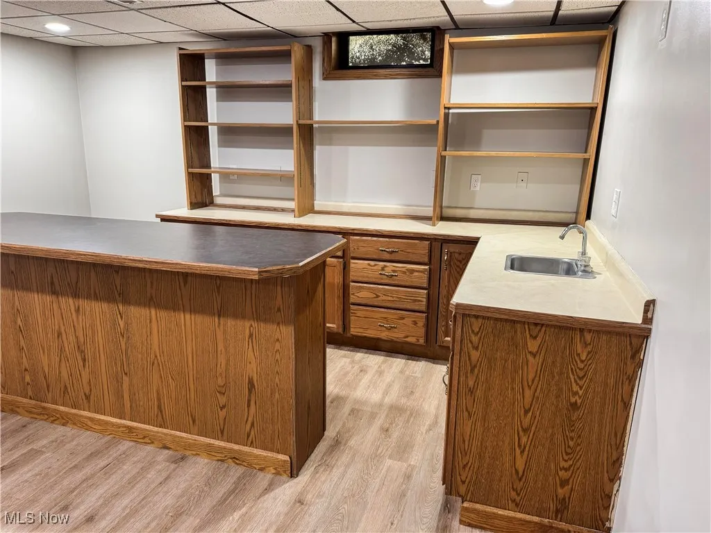 Wet bar with storage in the basement with a drop ceiling and light vinyl finished floors