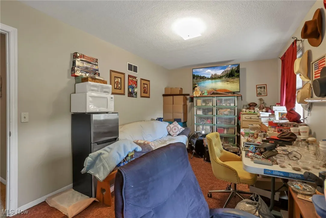 Carpeted bedroom with a textured ceiling and freestanding refrigerator