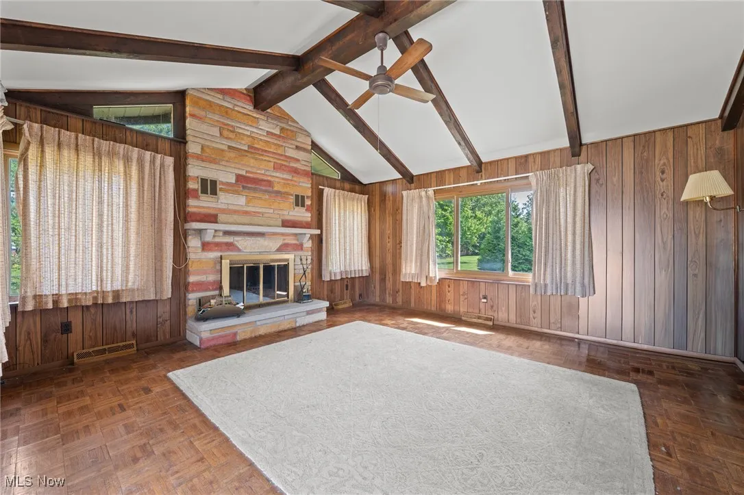 Unfurnished living room with wooden walls, a stone fireplace, and ceiling fan