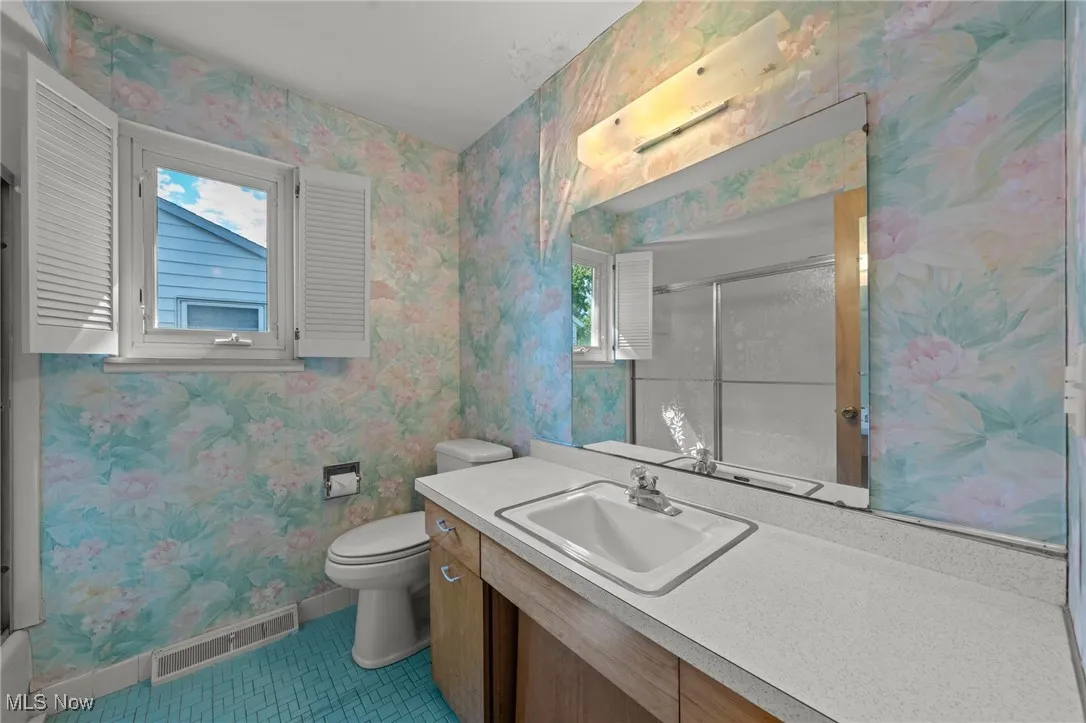 Full bath with wallpapered walls, vanity, a stall shower, and light tile patterned flooring