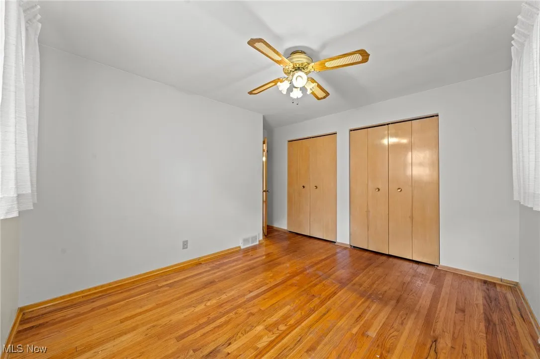 Unfurnished bedroom with hardwood / wood-style flooring, multiple closets, and a ceiling fan