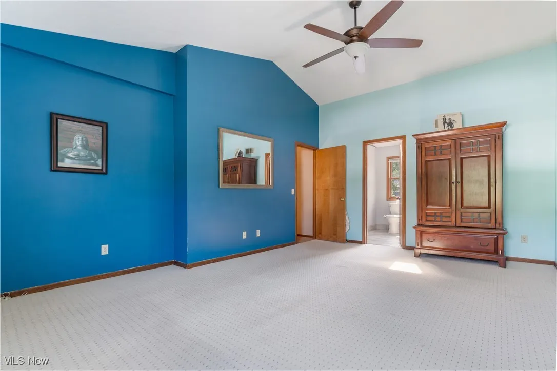Unfurnished bedroom featuring carpet, ceiling fan, ensuite bath, and high vaulted ceiling