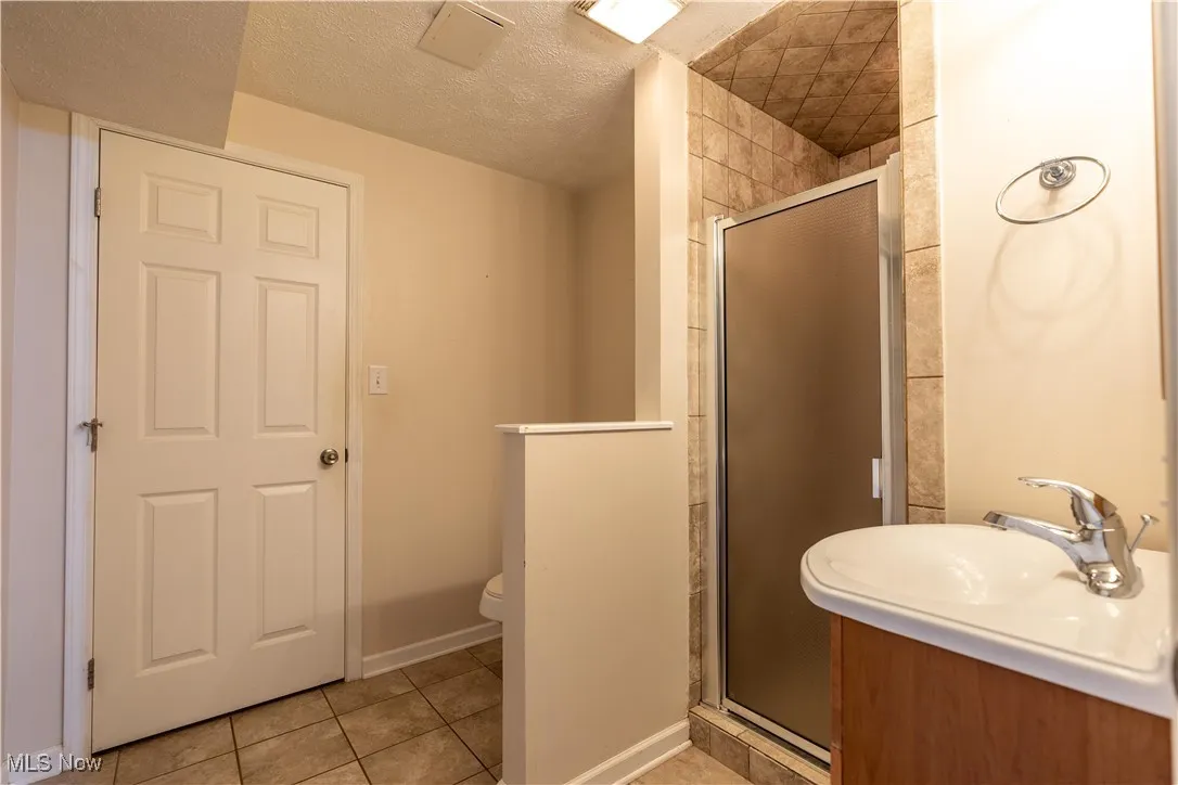 Bathroom with a textured ceiling, light tile patterned flooring, a shower stall, and vanity