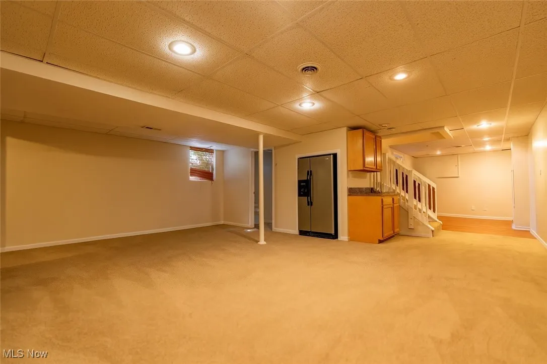 Below grade area with a paneled ceiling, stainless steel refrigerator with ice dispenser, light colored carpet, stairway, and recessed lighting